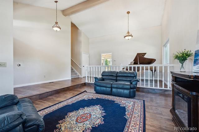 Living room with vaulted ceiling, blue leather sofas, patterned rug, and a piano beyond the railing.