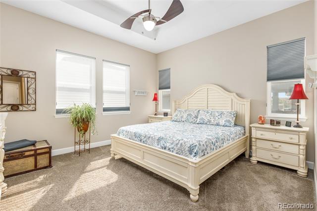 Bedroom with a cream bed, floral bedding, three window blinds, and a ceiling fan.