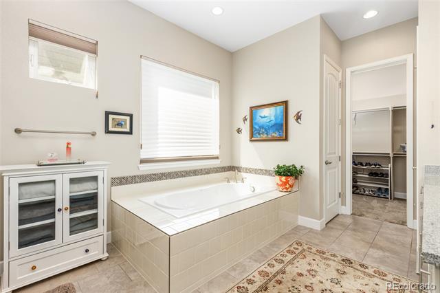 Bathroom with a large tiled soaking tub beside a glass-front cabinet and walk-in closet.