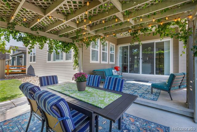 Furnished patio beneath a vine-covered pergola, with a dining table and blue cushioned chairs.