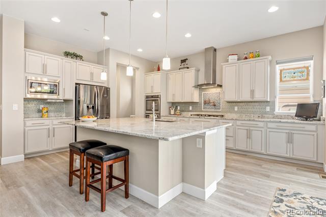 Bright kitchen with a large stone island, white cabinets, stainless appliances, and two bar stools.