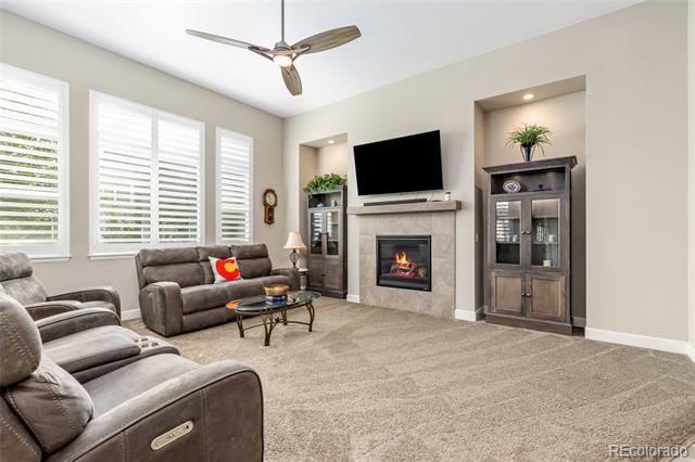 Living room with gray sectional seating, a gas fireplace, built-in cabinets, and shuttered windows.