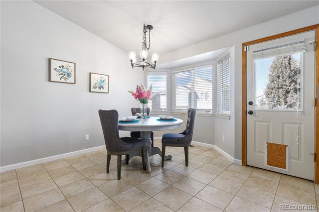Dining area with a round table, four chairs, chandelier, and tiled floor beside a glass-panel door.