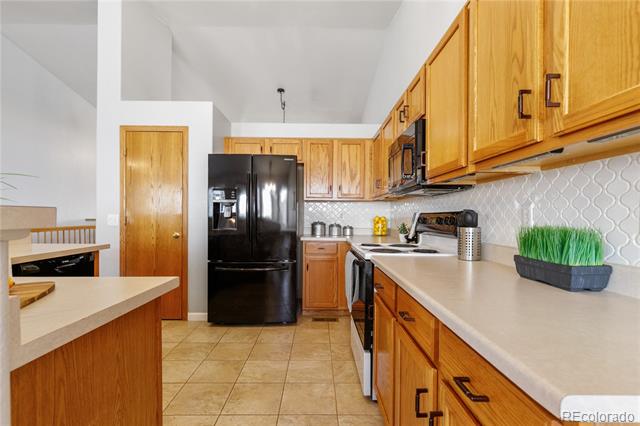 Kitchen with honey-colored cabinets, a black refrigerator, and a white patterned backsplash.