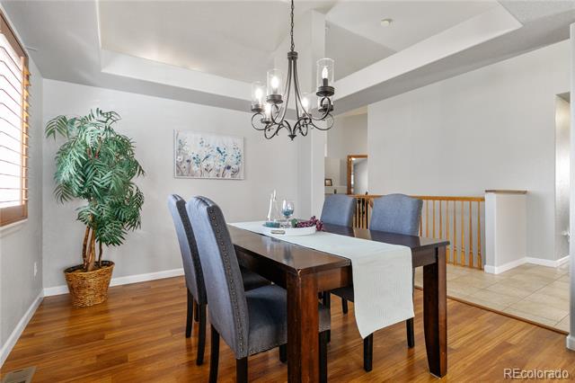Dining room with a dark wood table, blue chairs, black chandelier, and potted palm by a window.