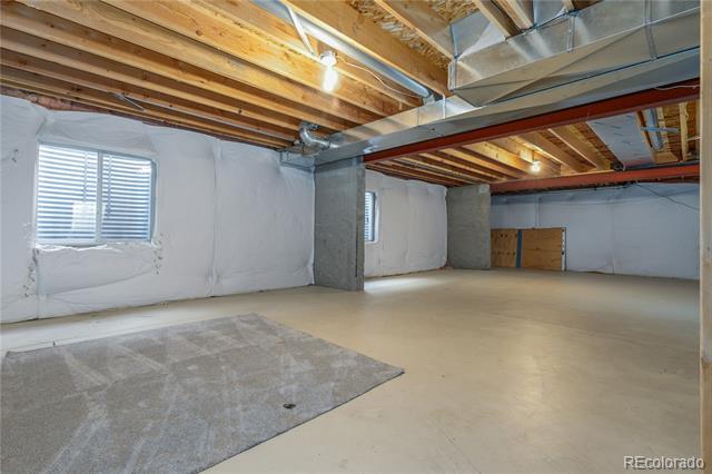 Unfinished basement with exposed ceiling joists and ductwork, small windows, and a gray rug.