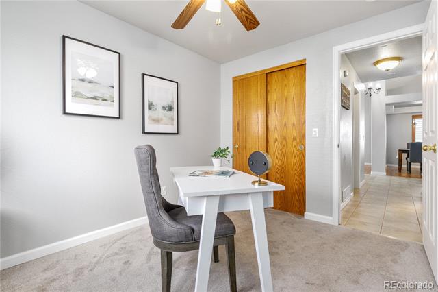 Home office with a white desk and gray chair beside wood closet doors and an open hallway.