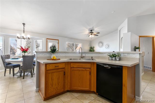 Open kitchen with honey-colored cabinets and black dishwasher beside a dining area with large windows.