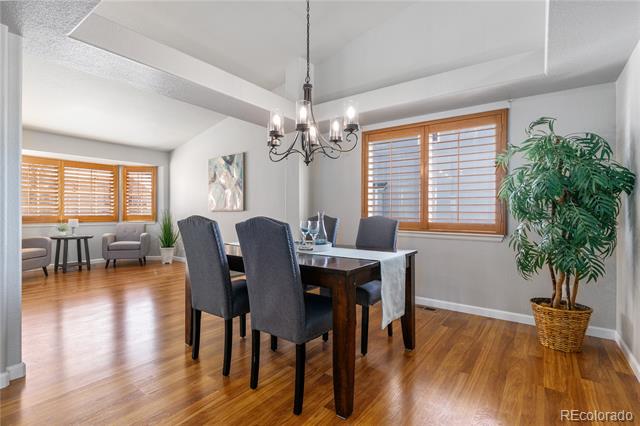 Dining room with hardwood floors, a dark dining table, chandelier, and windows with wooden blinds.