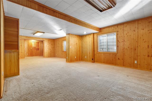 Vacant carpeted room with wood-paneled walls, a drop ceiling, and windows with blinds.