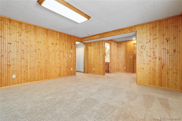 Empty carpeted room with honey-colored wood-paneled walls and open doorways.