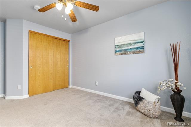 Carpeted bedroom with wooden closet doors, a ceiling fan, and simple neutral decor.