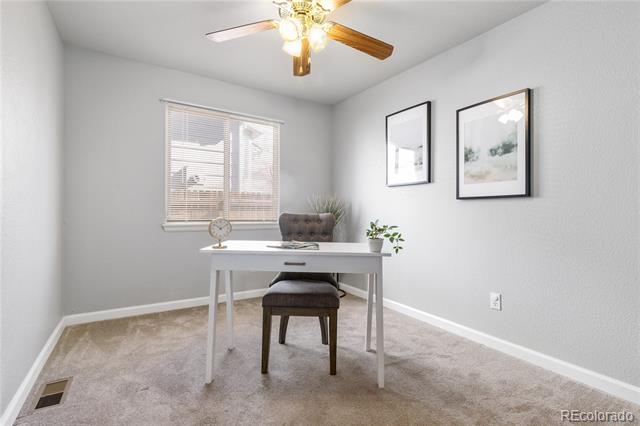 Staged home office with a white desk, dark chair, window blinds, and ceiling fan.