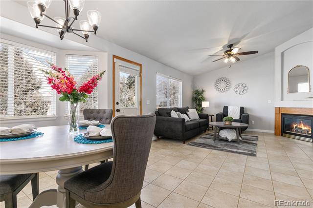 Open living and dining area with gray seating, tiled floors, and a lit fireplace.