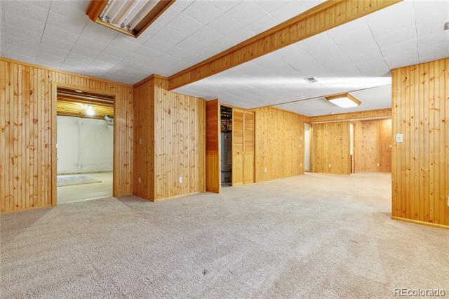 Empty wood-paneled basement rec room with beige carpet and doorways to adjoining rooms.