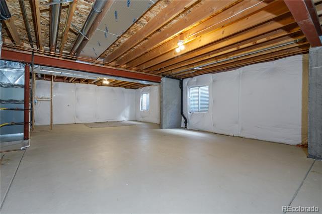 Unfinished basement with exposed ceiling joists, a concrete floor, and small windows.