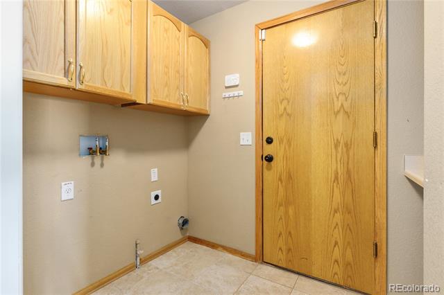 Empty laundry area with upper wood cabinets, appliance hookups, and a tiled floor.