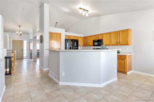 Open kitchen with honey-colored cabinets, a large gray peninsula, and beige tile flooring.