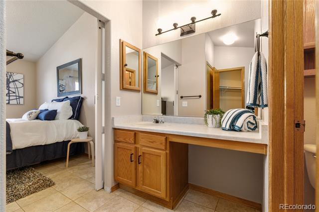 Bathroom vanity with wood cabinets and a large mirror, opening onto a furnished bedroom.