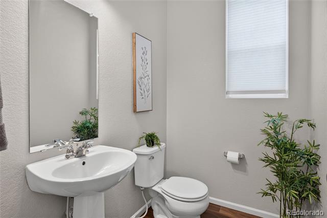 Bathroom with a white pedestal sink, toilet, large mirror, and window with blinds.