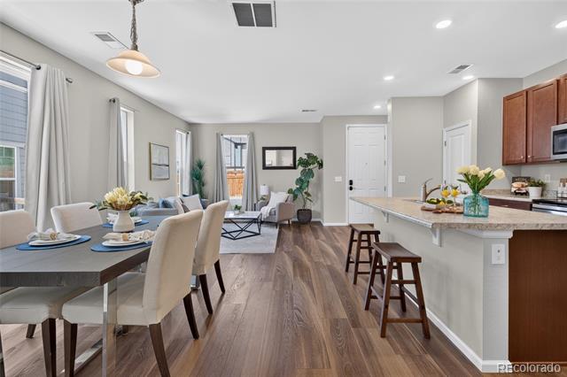 Open-plan dining room and kitchen with a long island, wood flooring, and neutral furnishings.