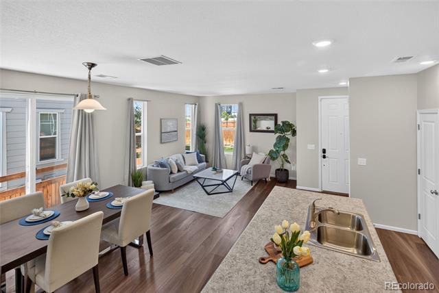 Open-plan kitchen and living room with a stone island, gray sofa, and dining area.
