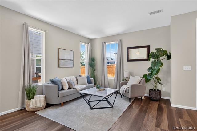 Staged living room with a gray sofa, glass coffee table, tall windows, and hardwood floors.