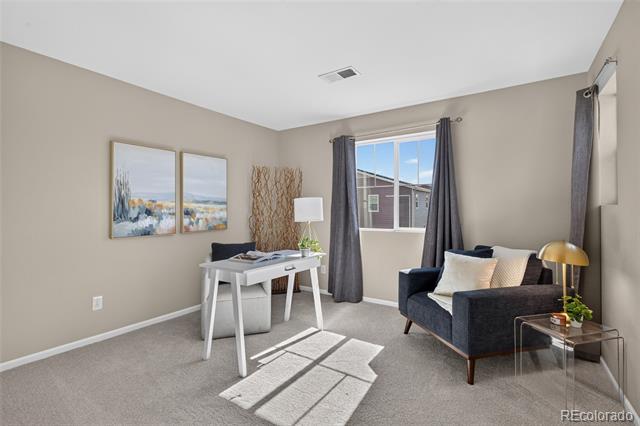 Staged home office with a white desk, dark armchair, framed artwork, and sunlight across the carpet.
