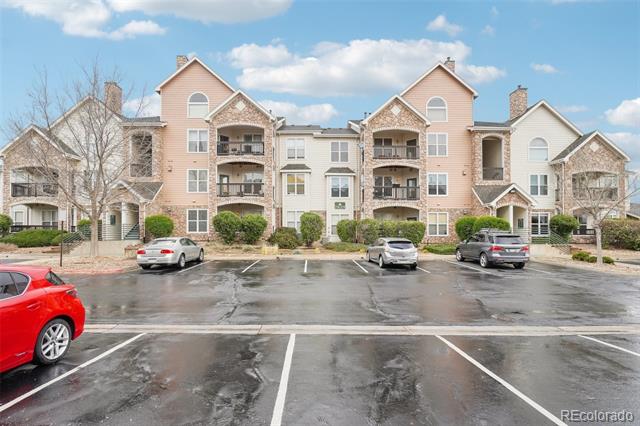 Condominium building with peach siding, stone accents, balconies, and a wet parking lot.