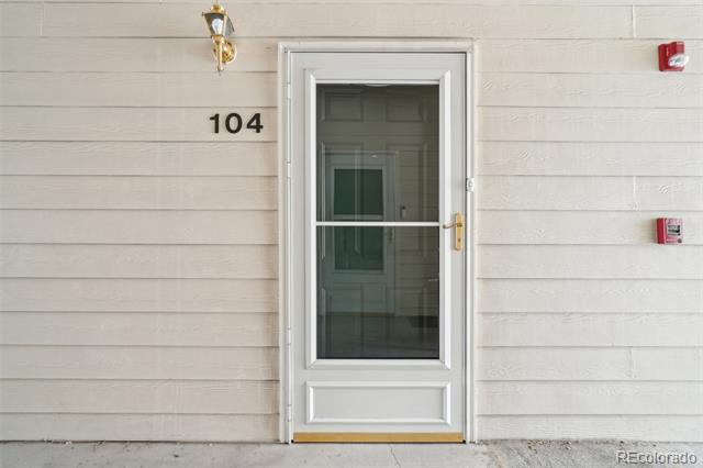 Unit 104 entrance with a white-framed glass storm door and light horizontal siding.