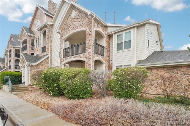 Residential building with stone facade, arched balconies, and shrubs along the sidewalk.