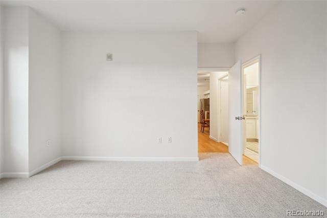 Empty carpeted room with white walls and open doorways to a hall and adjoining room.
