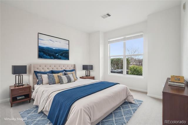 Bedroom with a white bed and blue runner, matching bedside tables, and a large window overlooking trees.