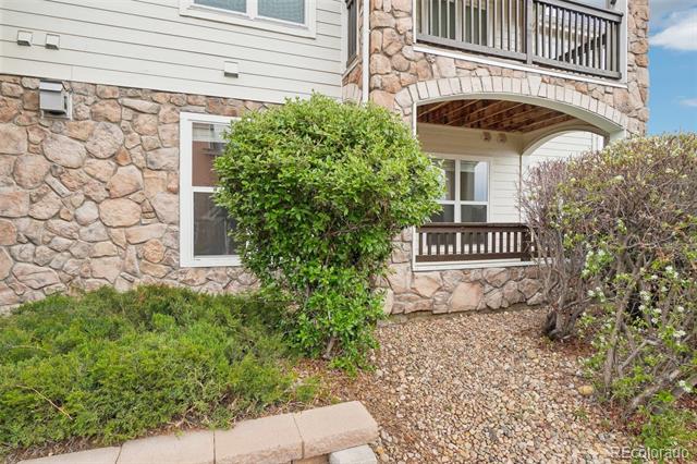 Residential building exterior with stone facade, balconies, shrubs, and a gravel walkway.