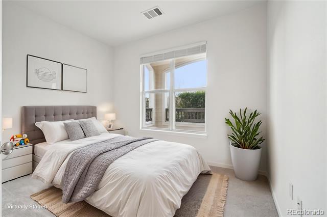 Bedroom with a gray tufted headboard, white bedding, and a large window overlooking greenery.