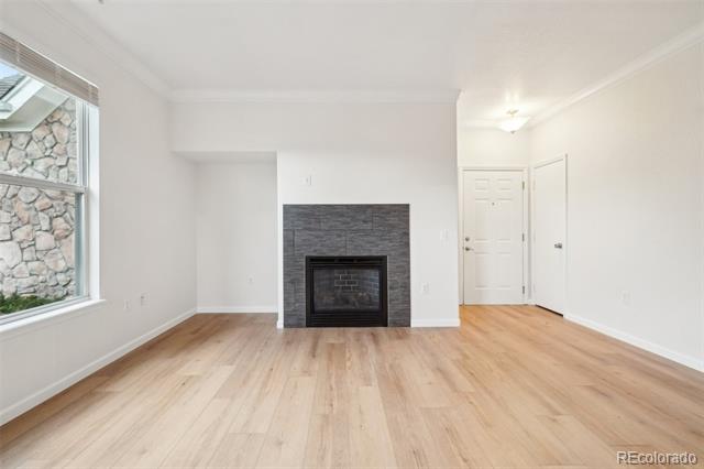 Vacant living room with a dark tiled fireplace, light wood floors, and a large window.