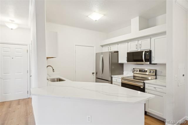 White kitchen with a large island, stainless steel appliances, and light wood flooring.
