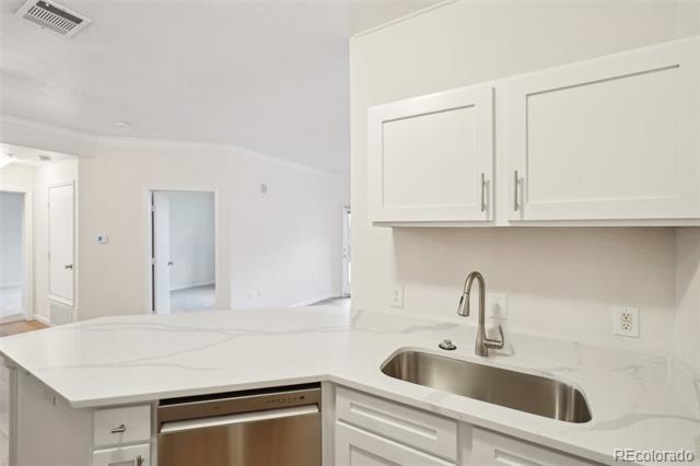 Vacant kitchen with white cabinets, a veined countertop, and a stainless-steel sink.