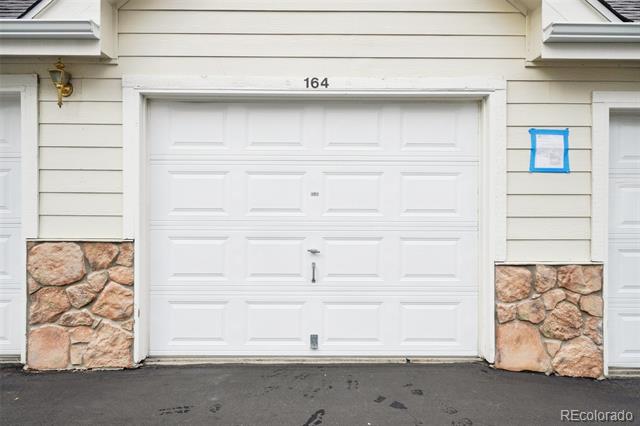 White paneled garage door numbered 164, set in beige siding above stone veneer.