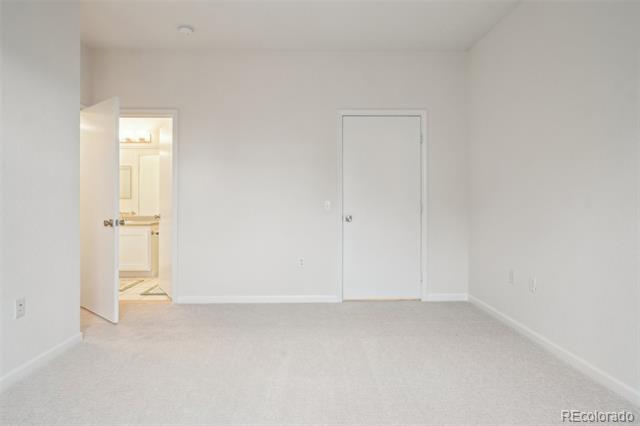 Empty carpeted bedroom with a closed door and an open doorway to a lit bathroom.