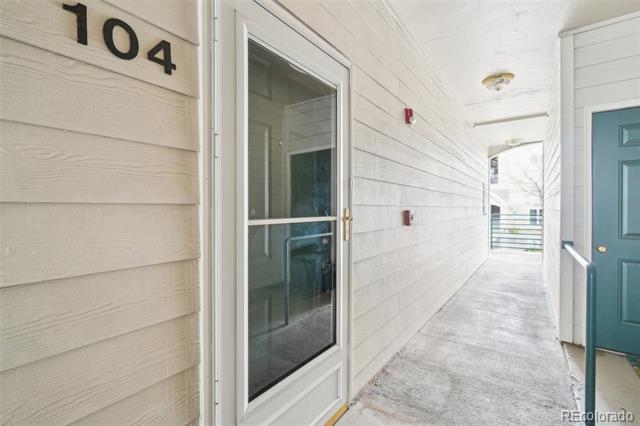 Covered walkway to Unit 104, with a glass storm door and teal door at the far end.
