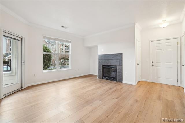 Empty living room with light wood floors, large windows, and a dark tiled fireplace.