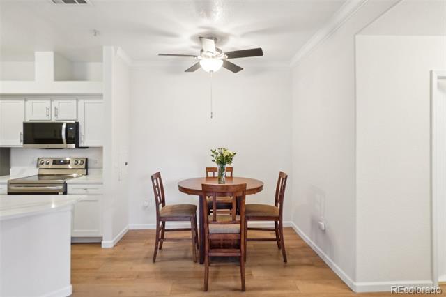 Dining area with a round wooden table and four chairs beside a white kitchen with stainless steel appliances.