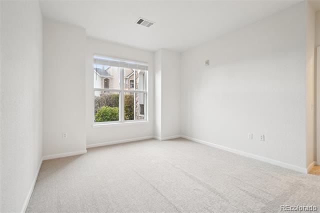 Vacant carpeted room with white walls and a window overlooking greenery.