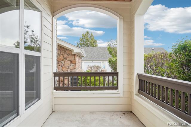 Covered balcony with dark wood railings overlooking neighboring homes and leafy shrubs.