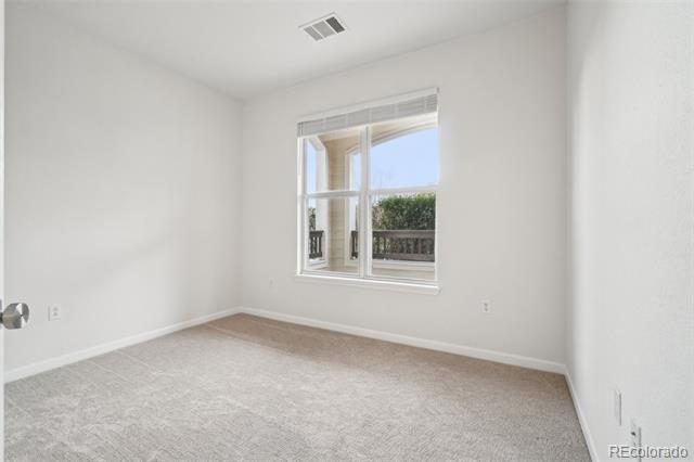 Empty bedroom with light carpet and a window overlooking a balcony and greenery.