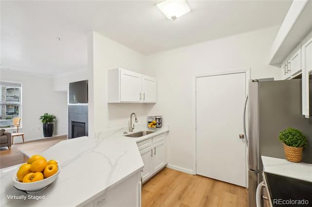 Virtually staged kitchen with a veined white peninsula, stainless refrigerator, and light wood floors.