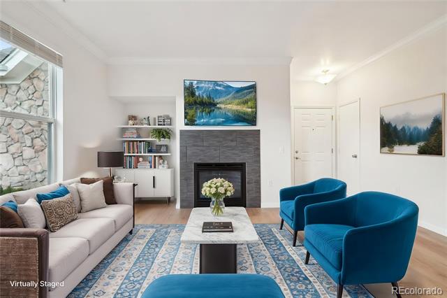 Living room with blue armchairs, a patterned rug, and a gray fireplace wall beneath a mountain-lake television.