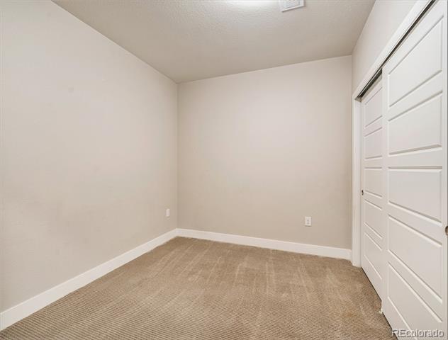 Empty carpeted bedroom with white closet doors and neutral walls.