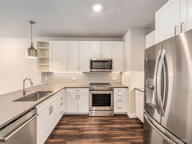 Kitchen with white cabinets, stainless steel appliances, subway tile backsplash, and dark wood-look floors.
